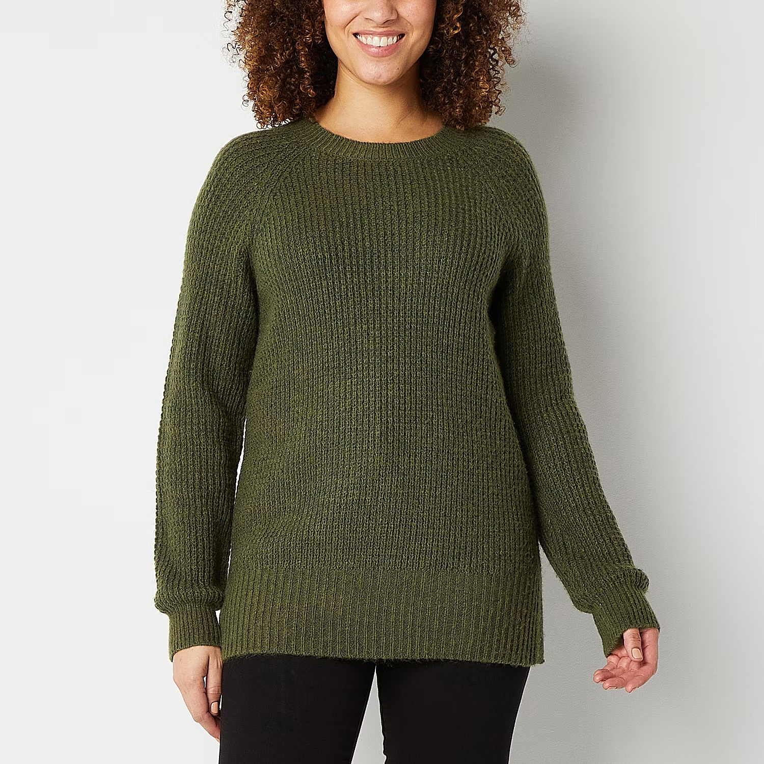 A woman wearing a green crew-neck sweater and black pants.