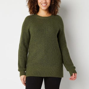 A woman wearing a green crew-neck sweater and black pants.