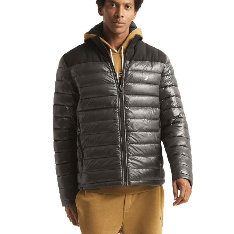 A man wears a Nautica Men's Quilted Jacket in dark gray with horizontal stitching and a front zipper. It's layered over a tan hoodie and features a high collar for added warmth.