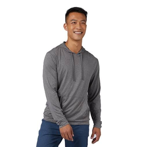 A smiling man wears a gray, long-sleeve hooded tee with drawstrings, paired with blue pants. The shirt has a casual fit and a front pocket.