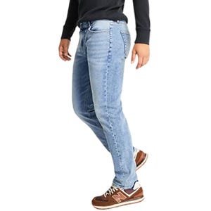 A person is wearing light blue jeans with a black top and brown New Balance sneakers.