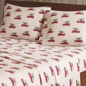 A bedding set with a holiday theme featuring red trucks carrying Christmas trees on a white background.
