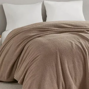 A beige, textured blanket is neatly spread over a bed with two white pillows against a light gray wall.