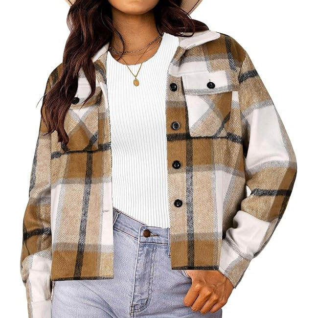 A woman wearing a brown and white plaid shacket over a white ribbed top and light blue jeans, accessorized with a gold necklace and wide-brimmed hat.