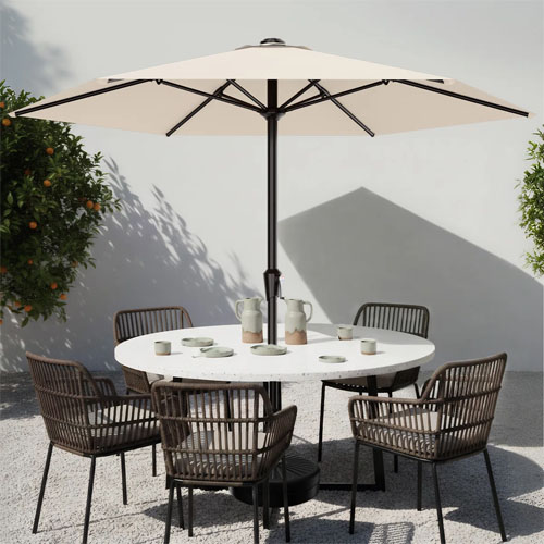 Outdoor patio setup with a white umbrella, round white table, and six brown wicker chairs. Tableware includes cups and pitchers.