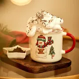 A festive mug with a snowman and Christmas tree design, filled with a creamy beverage topped with whipped cream and chocolate shavings, is set on a wooden tray beside a small star-shaped dish containing ground coffee or cocoa.