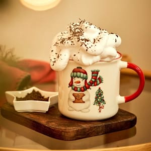 A festive mug with a snowman and Christmas tree design, filled with a creamy beverage topped with whipped cream and chocolate shavings, is set on a wooden tray beside a small star-shaped dish containing ground coffee or cocoa.