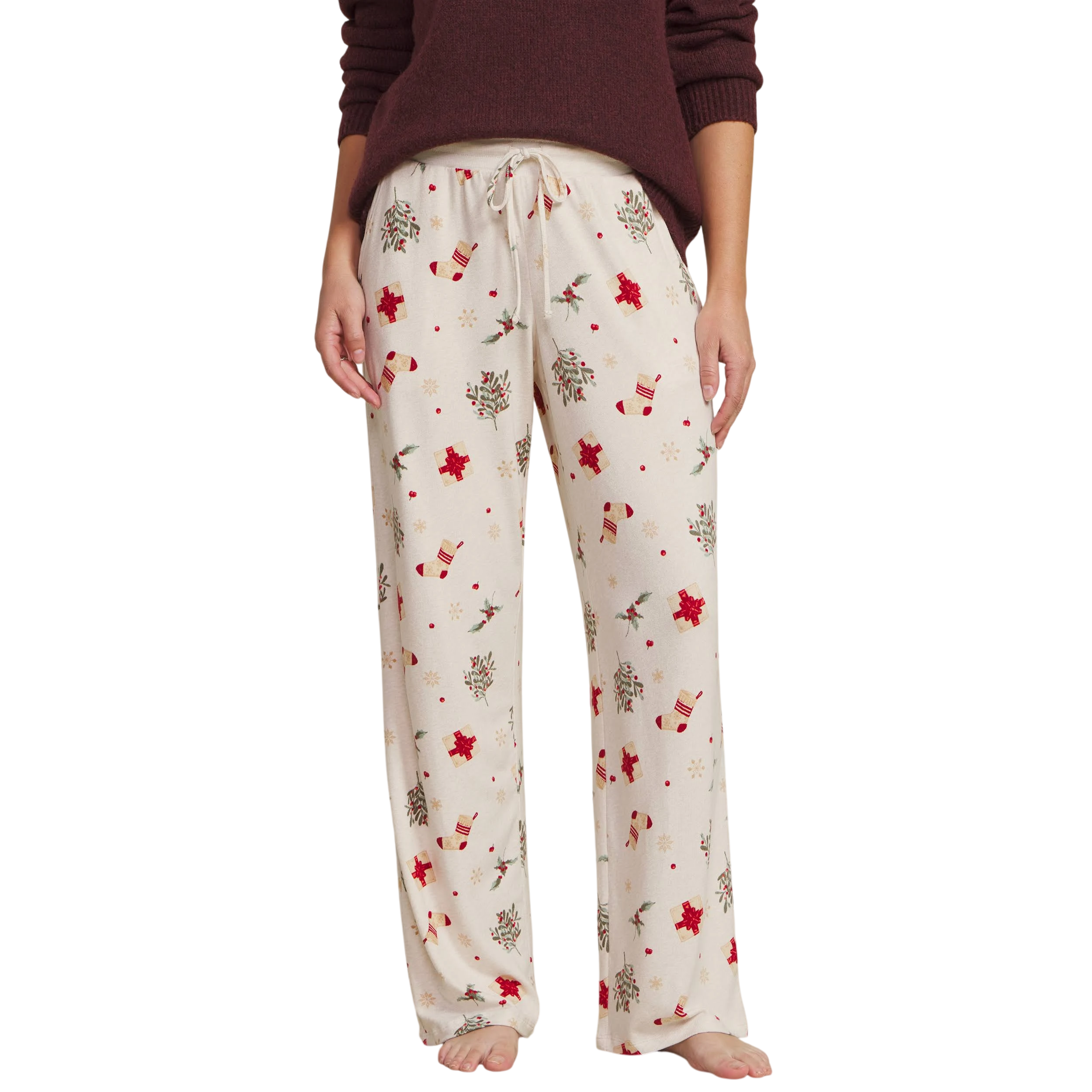 Cream-colored pajama pants with a festive holiday print featuring red gift boxes, stockings, holly, and snowflakes.