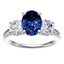 A ring features a large, oval blue sapphire flanked by two smaller round diamonds, all set in a shiny metal band.