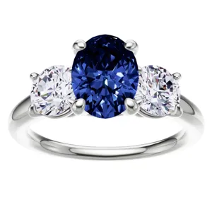 A ring features a large, oval blue sapphire flanked by two smaller round diamonds, all set in a shiny metal band.