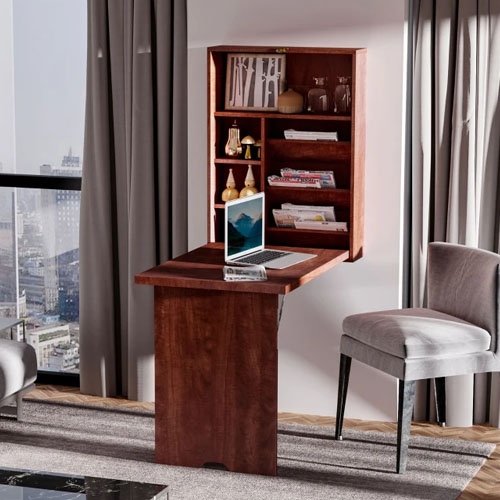A wall-mounted shelving unit with a fold-down desk and laptop, next to a grey upholstered chair.