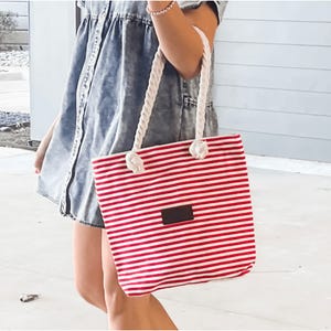 Red and white striped canvas tote bag with sturdy rope handles tied in knots, featuring a dark rectangular patch on the front; measures 14 inches in height.