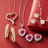 Assorted jewelry on a red background, featuring heart-shaped pendants with gemstones, gold hoop earrings with diamonds, and matching heart earrings with a red gift box.