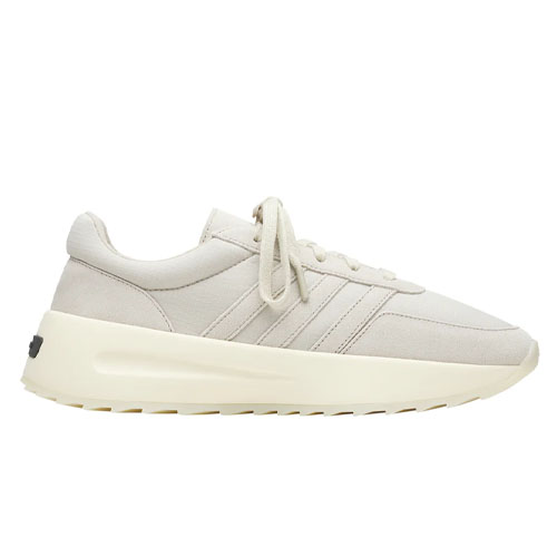 The Adidas x Fear of God sneakers feature a minimalist design in a light beige color with subtle Adidas stripes, a chunky cream sole, and laces for closure, offering a stylish and modern look.