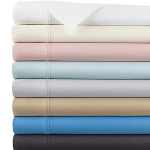 A stack of neatly folded bed sheets in various colors including white, cream, pink, light blue, gray, beige, blue, and dark gray.