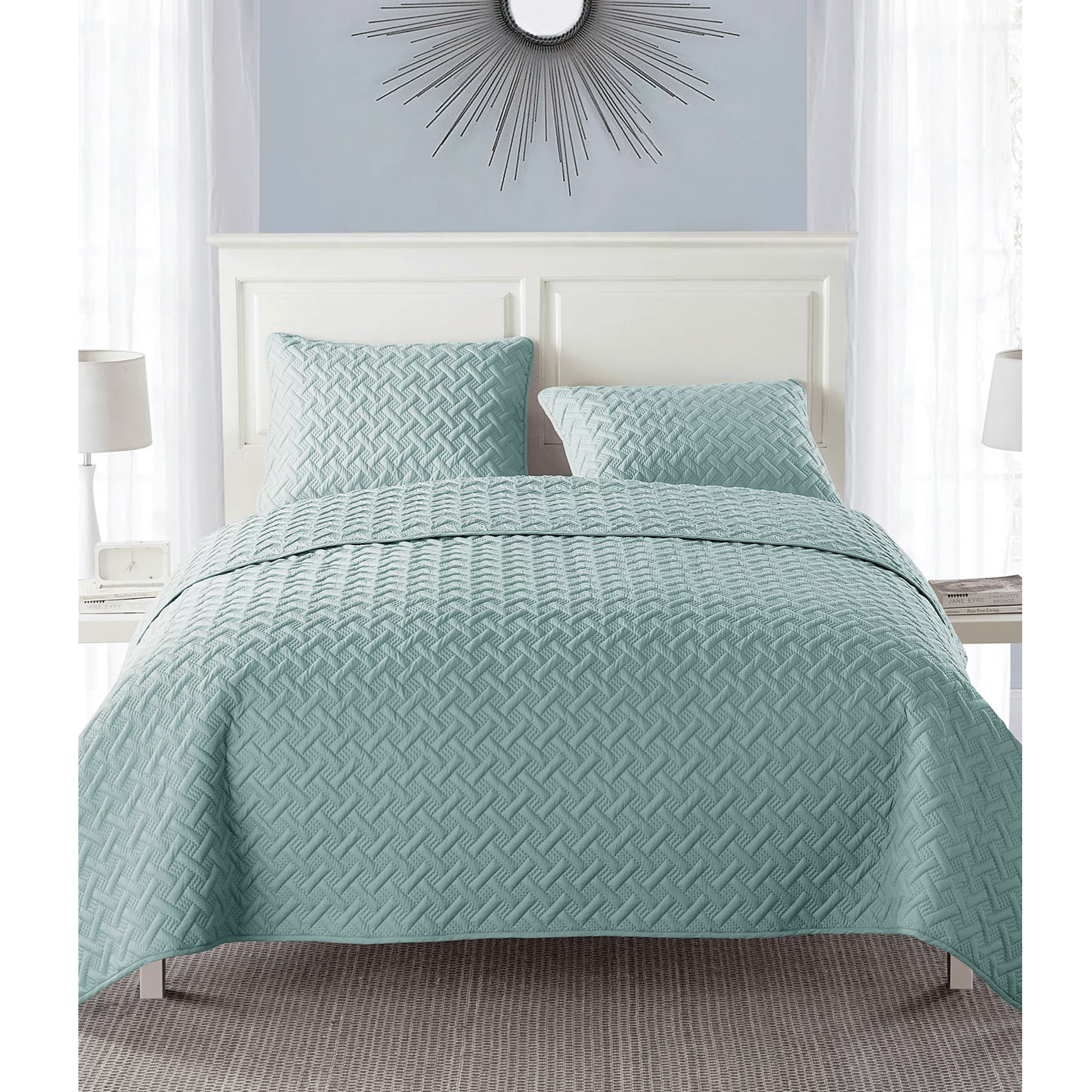 A bedding set featuring a light teal quilt with a geometric pattern and matching pillow shams on a bed. Includes a white headboard, two bedside lamps, and a decorative wall mirror.