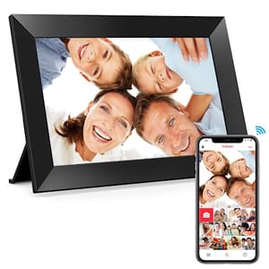 A black digital photo frame displaying a photo of a smiling family, alongside a smartphone using the Frameo app to send pictures to the frame.
