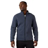 A man is wearing a navy blue zip-up jacket with a high collar, casually styled over a white shirt and black pants.