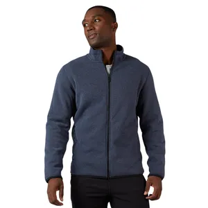 A man is wearing a navy blue zip-up jacket with a high collar, casually styled over a white shirt and black pants.