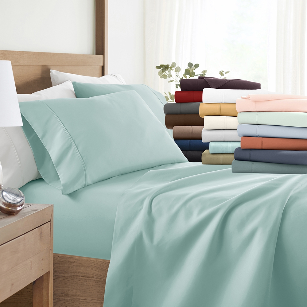 Assorted colors of bed sheets and pillowcases displayed on a bed and stacked neatly to the side.
