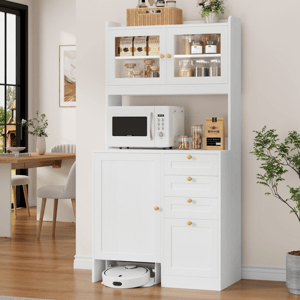 A white kitchen cabinet with storage space holds a microwave, jars, and a coffee pack. A robot vacuum is stored in the bottom compartment. The scene includes a nearby dining area with chairs and a table, and a potted plant is visible.