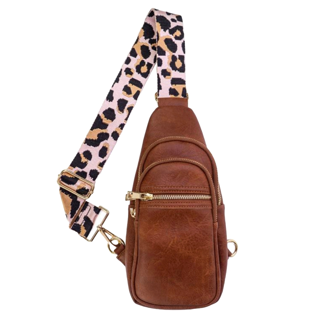 Brown leather sling bag with two front zippered compartments and a gold zipper. Features an adjustable strap with a pink and black leopard print pattern.