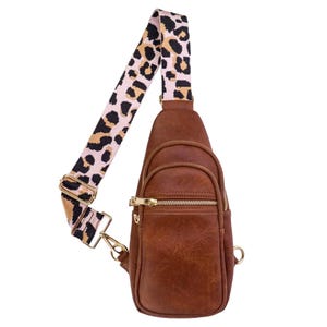 Brown leather sling bag with two front zippered compartments and a gold zipper. Features an adjustable strap with a pink and black leopard print pattern.