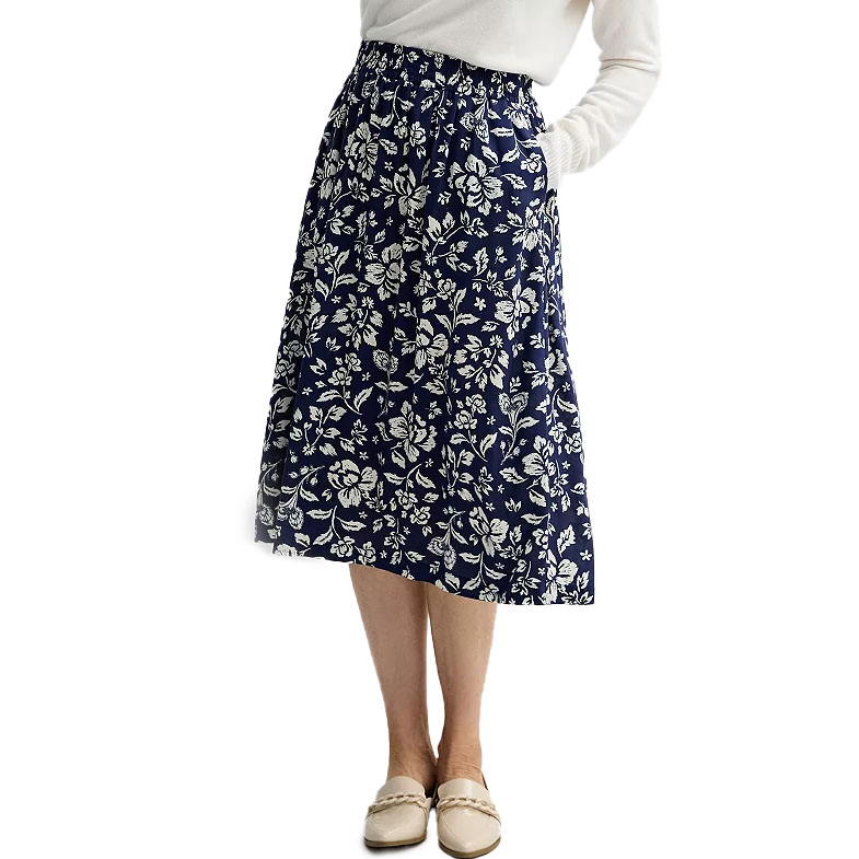 A woman wears a knee-length navy skirt with white floral patterns, paired with a white top and beige loafers.