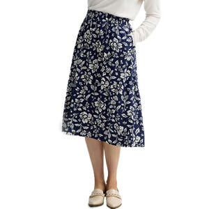 A woman wears a knee-length navy skirt with white floral patterns, paired with a white top and beige loafers.