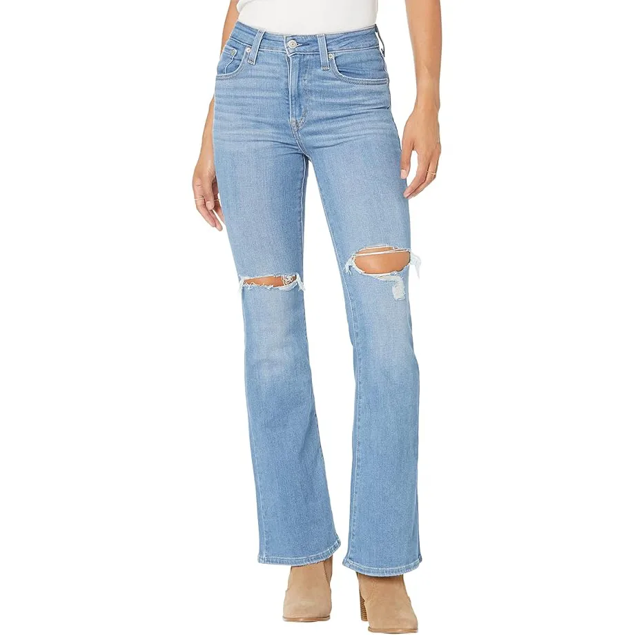 Light blue high-rise flare jeans from Levi's with ripped details at the knees, featuring a classic five-pocket design and button-zip closure, paired with tan heeled boots.
