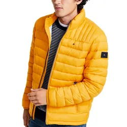 A man is wearing a bright yellow quilted jacket with small logo patches on the chest and sleeve. Underneath, he has on a black and white patterned sweater.