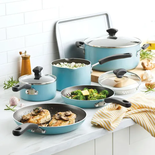 A set of light blue cookware including pots, pans, and a baking sheet with cooked meals on the countertop.