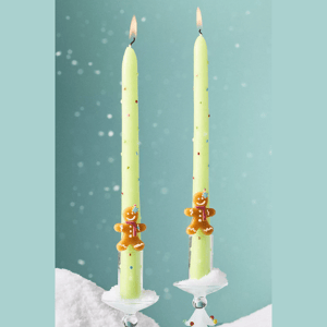 Two light green candles with colorful sprinkles and gingerbread figure decorations, set in clear holders with a snowy base.