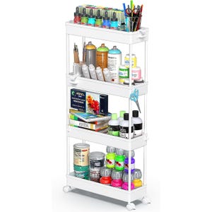 A four-tier rolling cart holds various art supplies including paint bottles, markers, scissors, brushes, and glue. Each tier contains items like spray paint, acrylics, watercolor sets, and art books.