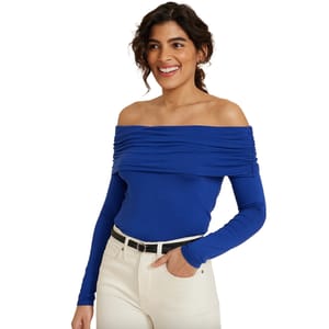 A woman wears a blue off-the-shoulder top with long sleeves, paired with white pants and a black belt.