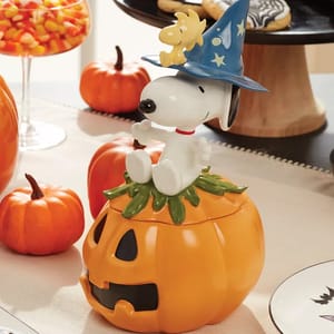 A ceramic Halloween-themed container featuring a character in a blue wizard hat sitting on a carved pumpkin, surrounded by decorative pumpkins and candy on a festive table setting.
