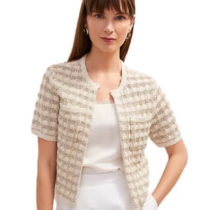 A woman is wearing a short-sleeved, textured beige cardigan over a white top, paired with white bottoms.