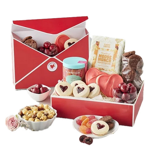 The Harry & David Valentine’s Day Box features heart-shaped cookies, chocolate-covered cherries, a jar of candy, gourmet caramel popcorn, a small bowl of colorful gummies, and cookies, all packaged in a red box designed like an envelope.