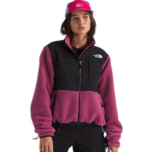 The North Face Denali Retro Jacket features a pink fleece body with black panels on the chest and shoulders, a full front zipper, zippered pockets, and an elastic hem and cuffs, showcasing a vintage style with a modern fit.