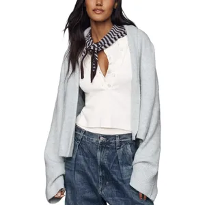 A person wears a white buttoned top and dark jeans with a light gray cardigan draped over their shoulders. A striped scarf is tied around the neck.