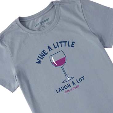 A gray women's t-shirt with the phrases \“Wine a little, Laugh a lot\“ and a graphic of a wine glass in pink and purple tones.