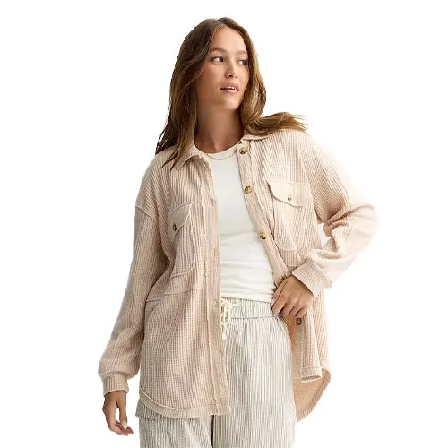 A woman in a beige button-up shirt with chest pockets, layered over a white top, paired with light, striped pants.