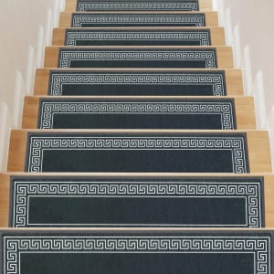 Stair treads with a Greek key pattern on dark fabric, set on light wooden steps.