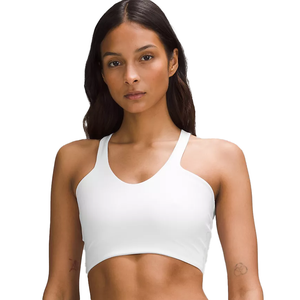 A woman is wearing a white sports bra with thin shoulder straps. She has long hair and a tattoo on her arm.