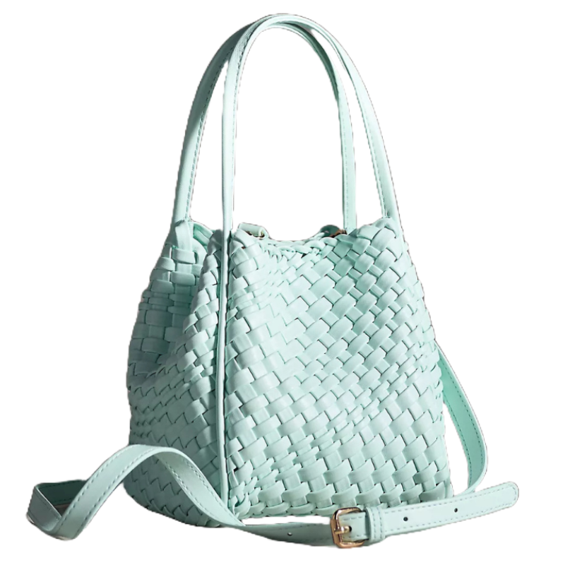The Anthropologie Hollace Tote is a light blue woven bag featuring dual handles and an adjustable strap with a metal buckle, suitable for versatile styling.