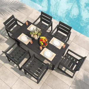 A poolside dining setup with a black table and eight matching chairs. The table is set with plates, glasses, and a centerpiece featuring flowers and a bowl of colorful fruit.