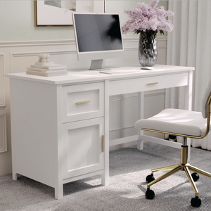 A white desk with a computer, keyboard, mouse, and a vase of purple flowers sits on a gray carpet. The desk features gold handles and is paired with a white chair with gold accents.