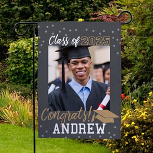 Graduation garden flag featuring a photo of a graduate in a cap and gown, with text \“Class of 2025\“ and \“Congrats! Andrew,\“ displayed in a garden setting.