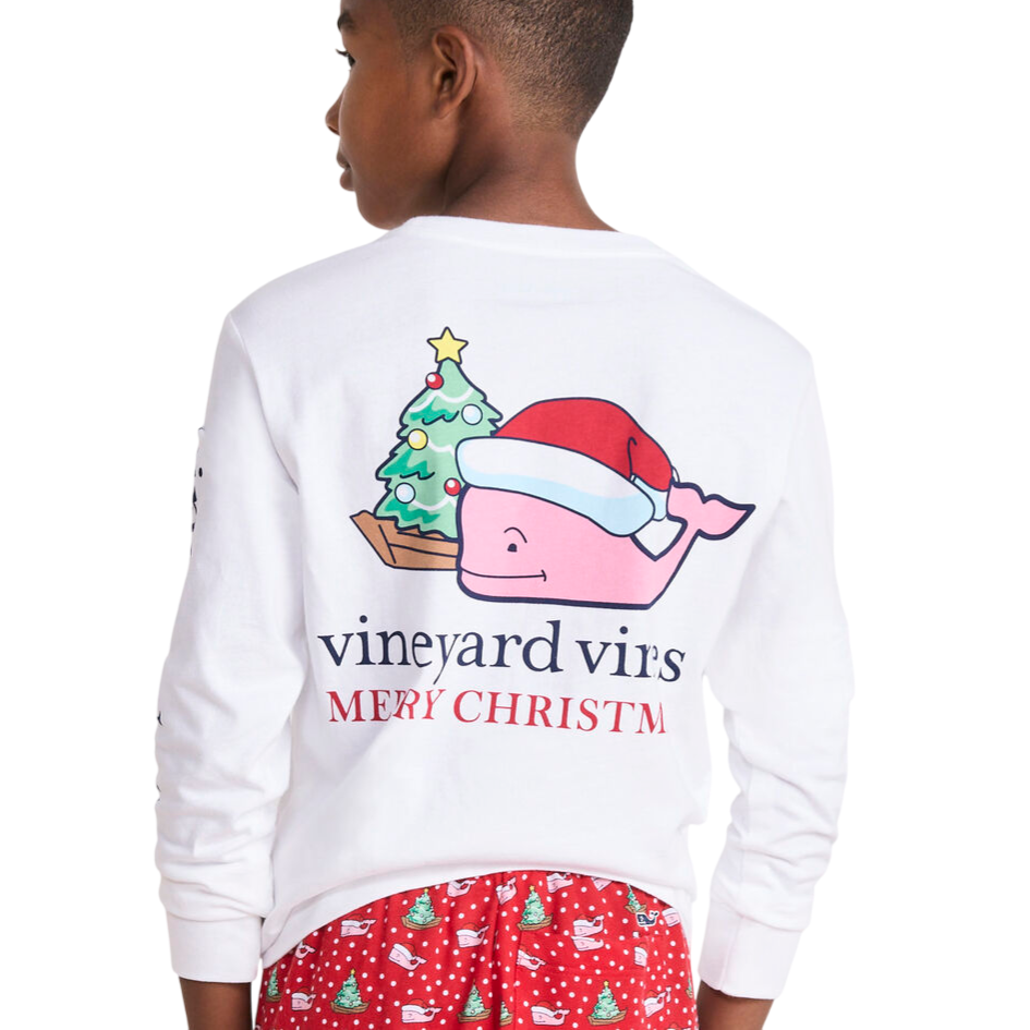 Boy wearing a white long-sleeve shirt featuring a pink whale in a Santa hat with \“Merry Christmas\“ text, paired with red pajama bottoms decorated with Christmas trees and whales.