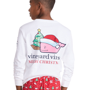 Boy wearing a white long-sleeve shirt featuring a pink whale in a Santa hat with \“Merry Christmas\“ text, paired with red pajama bottoms decorated with Christmas trees and whales.